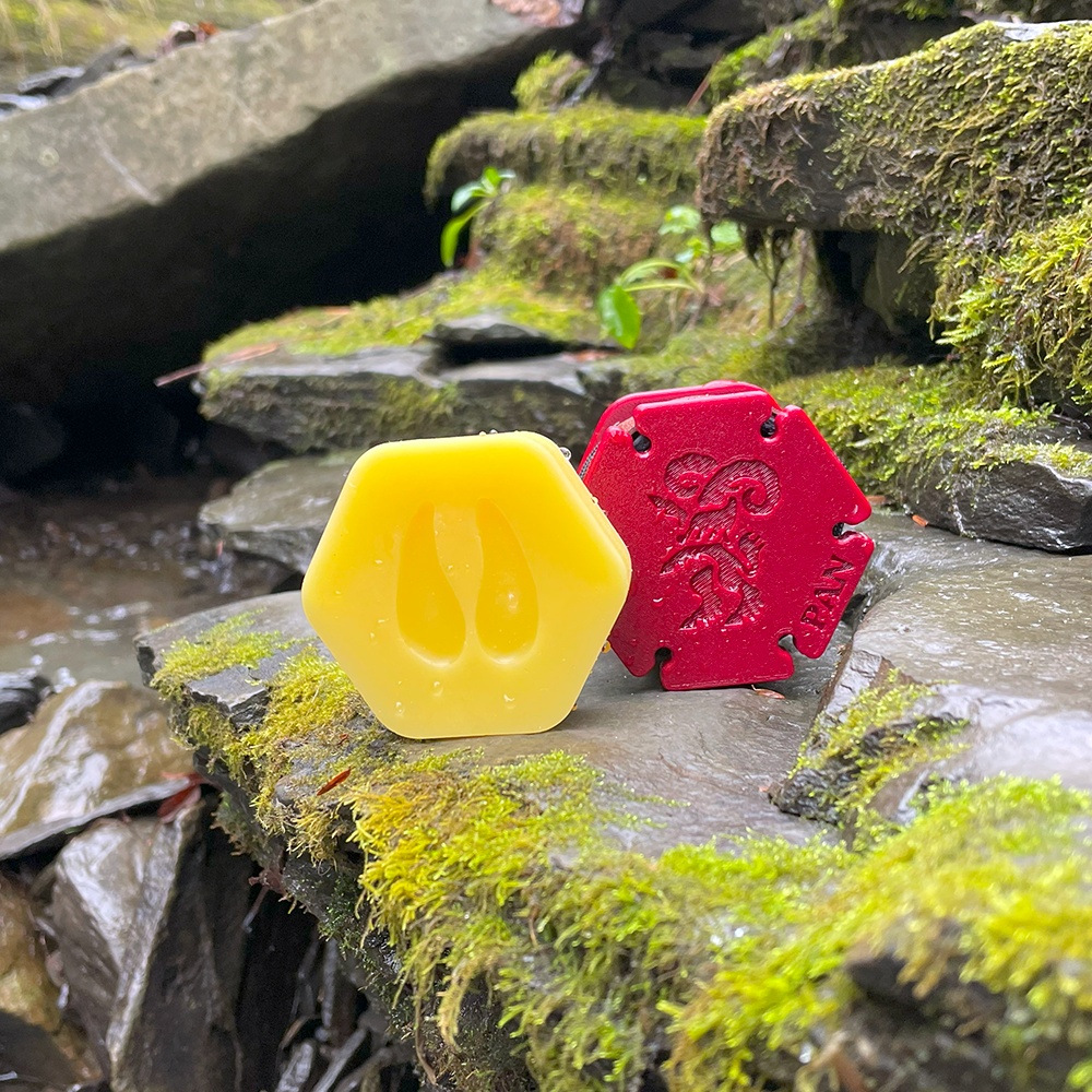 Pan's Sling Wax, a fabric wax, and Pan sling sitting together on a rocky ledge near a small brook.